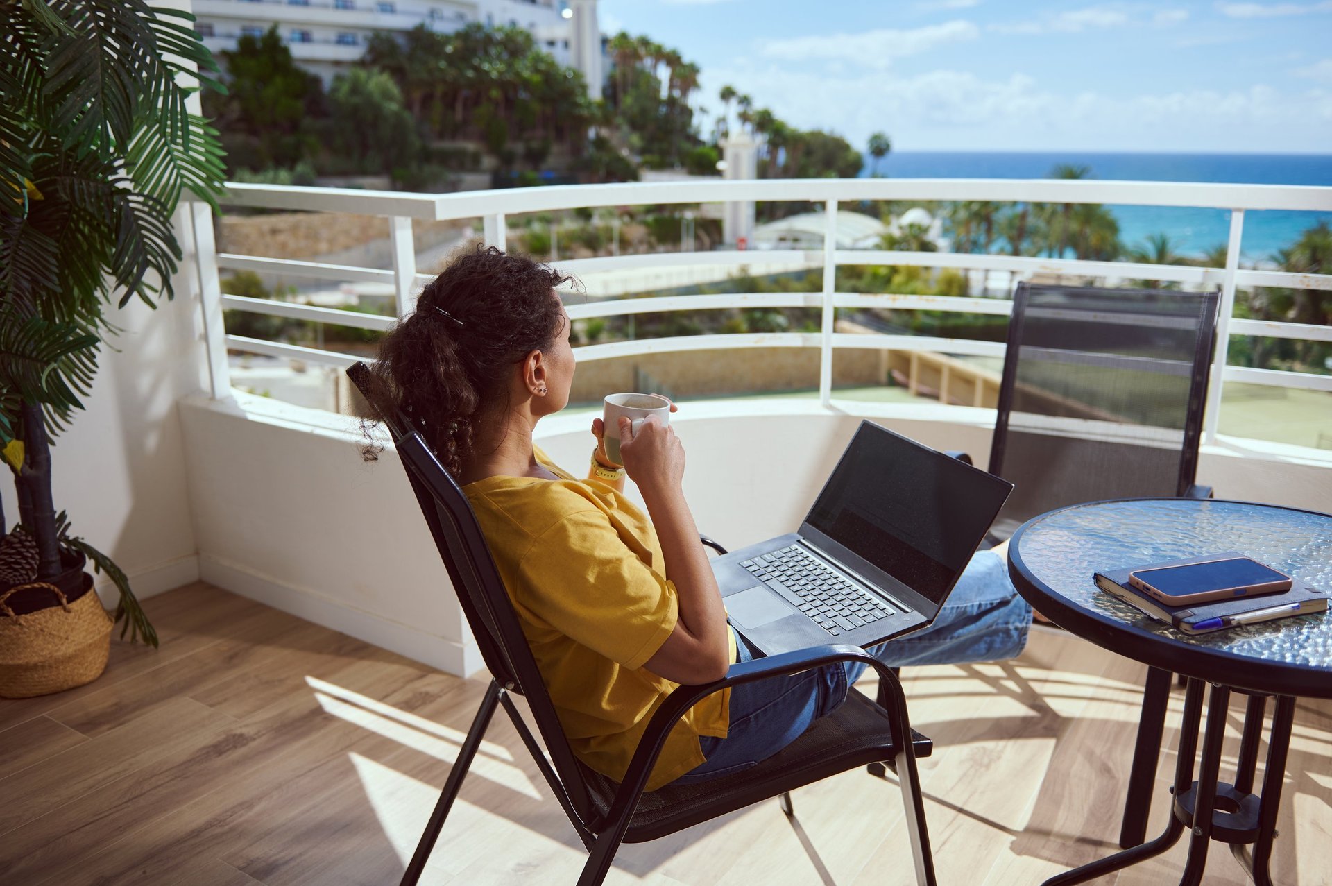 Woman working remotely on laptop from beautiful tropical beach with ocean views